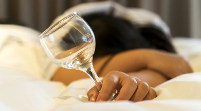 Mulher dormindo com uma taça na mão | Malefícios do álcool para o sono